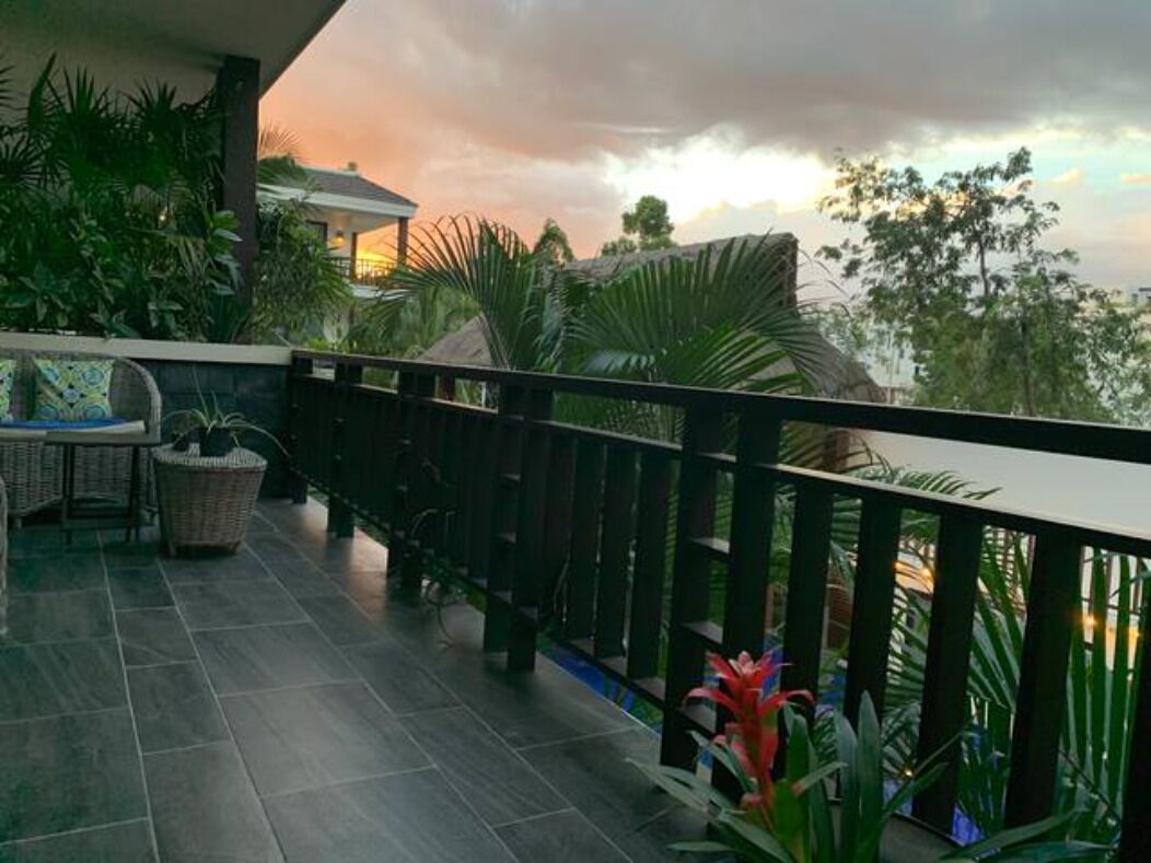 Un balcón con vista a la puesta de sol, rodeado de plantas tropicales y una mesa de mimbre.