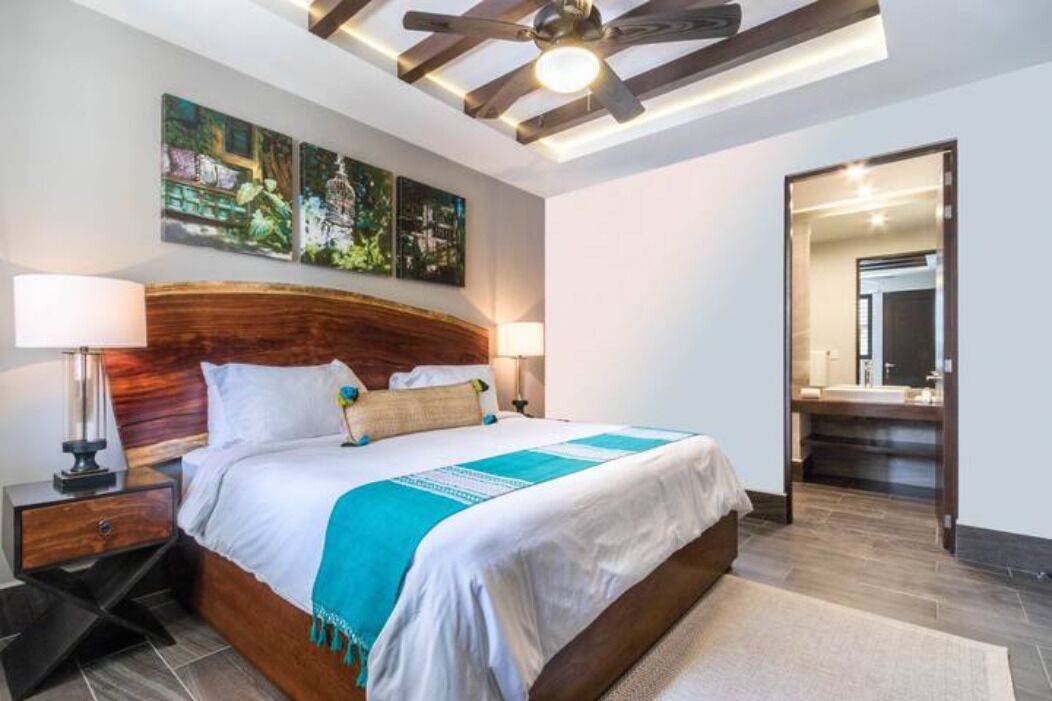 A bedroom with a wooden headboard, a large bed, two bedside lamps, and a ceiling fan.