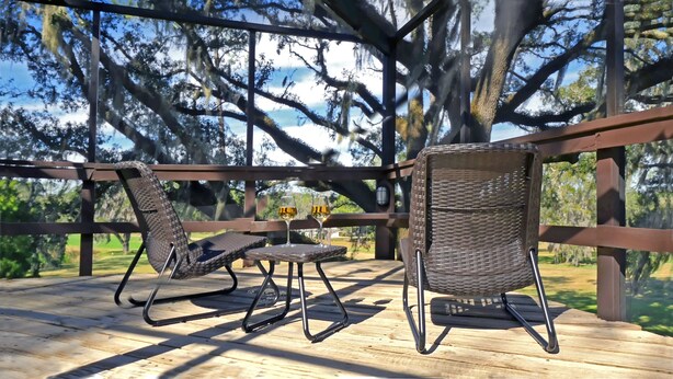 Una terraza de madera con sillas de mimbre y una pequeña mesa, rodeada de árboles.