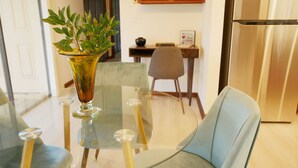 Un comedor con una mesa de vidrio, un florero con hojas verdes y una silla.