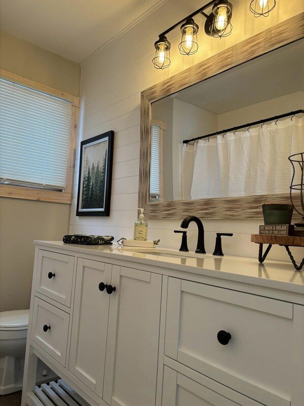 A bathroom with a white vanity, a large mirror, and a light fixture above the mirror.