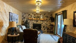 Un salon chaleureux avec une cheminée en pierre, des murs en bois, un canapé confortable et une petite table d’appoint.