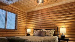 Une chambre dans un chalet en bois, avec un lit, deux lampes de chevet et une fenêtre avec des stores.