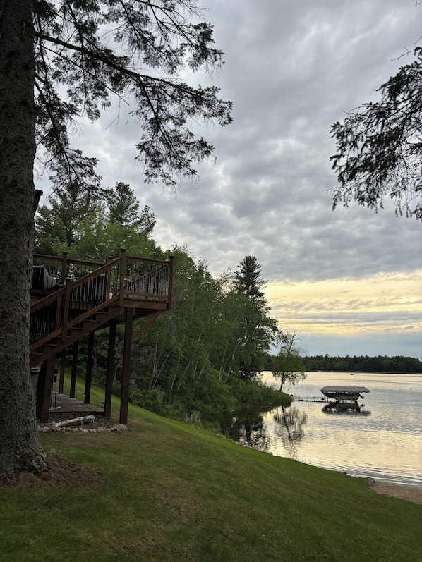 A wooden deck with a railing overlooking a lake, surrounded by trees.