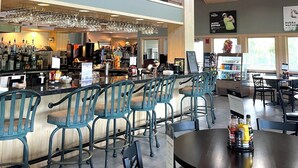 Un ristorante con zona bar, posti a sedere e un soffitto alto con travi in legno.