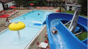 Una piscina con uno scivolo acquatico, lettini e ombrelloni.