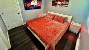 Een slaapkamer met een bed, een aan de muur bevestigde televisie, een plafondventilator en een nachtkastje met een lamp.