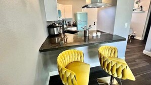 Een moderne keuken met een centraal kookeiland, twee gele bekleden stoelen en een roestvrijstalen afzuigkap.