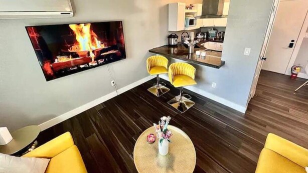 Een moderne woonkamer met een flatscreen televisie, twee gele fauteuils, een ronde salontafel en een plafondventilator.