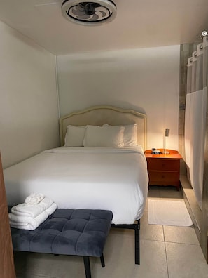 Une chambre d’hôtel avec un lit, une table de chevet, une lampe et un petit banc.
