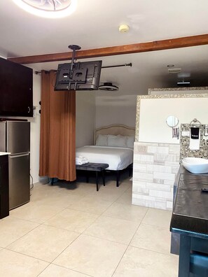 Une pièce de taille modeste comprenant un lit, une petite table, un lavabo encastré et un téléviseur fixé au mur.