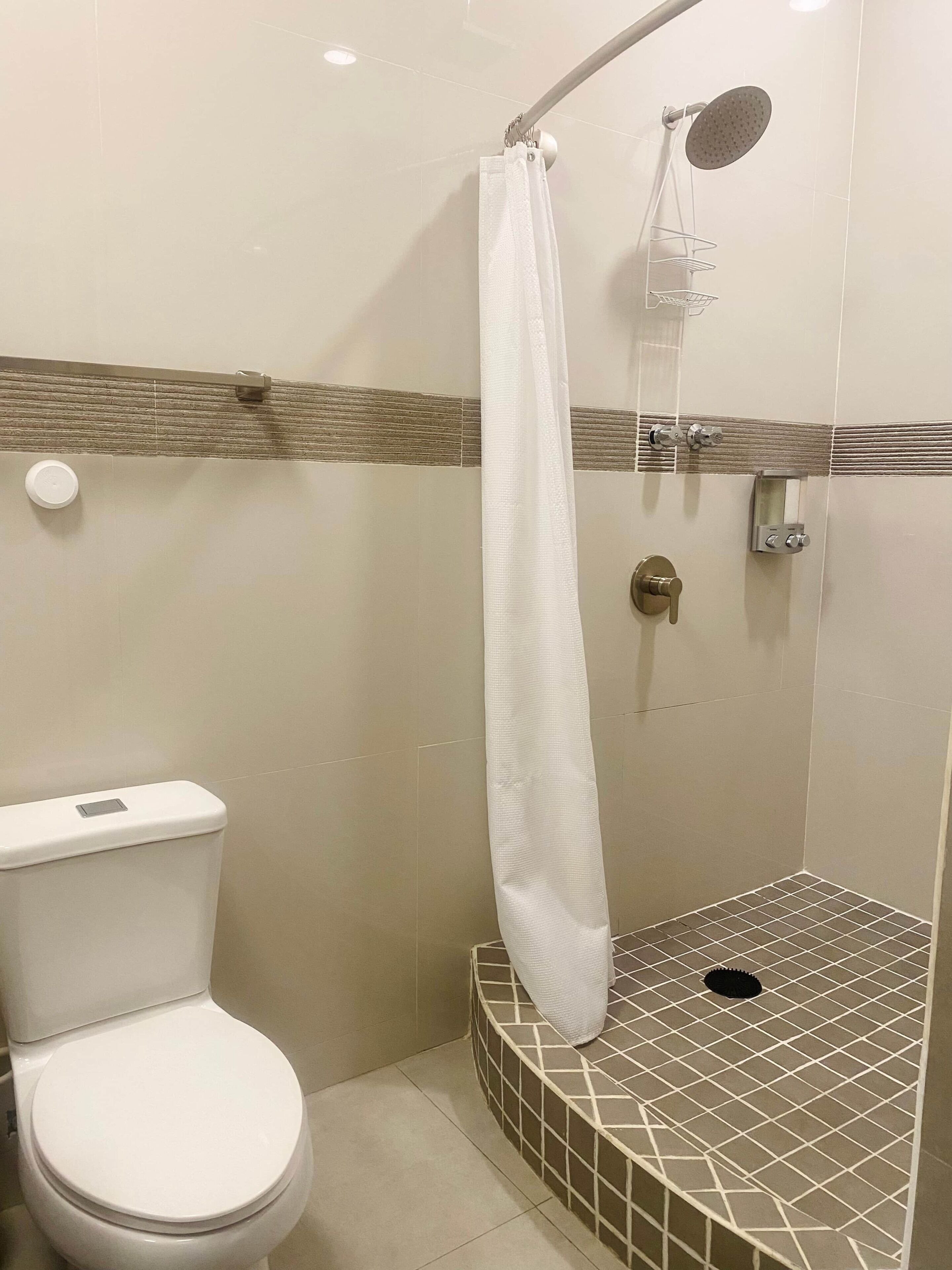A bathroom with a toilet, a shower with a curved showerhead, and a tiled floor.
