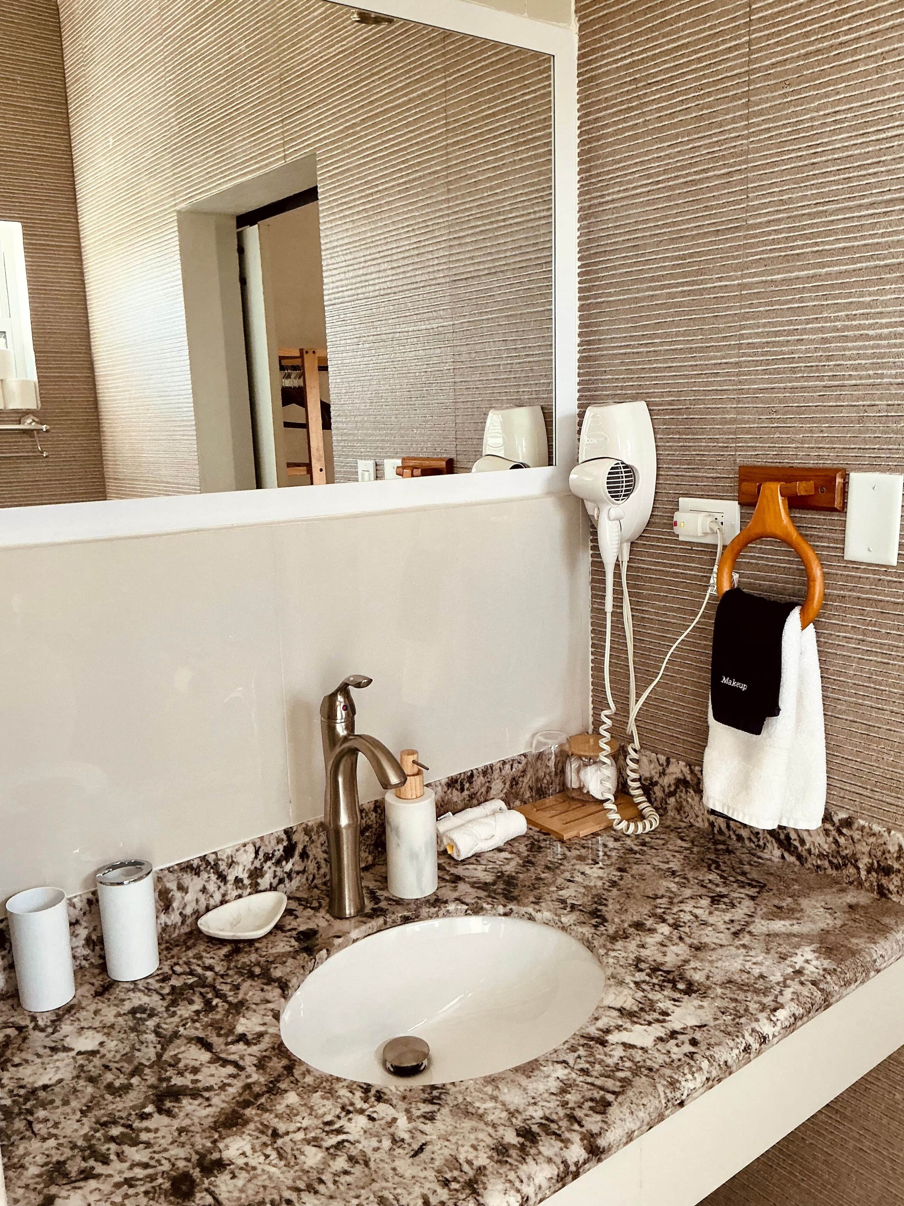 A bathroom with a granite countertop, a white sink, a mirror, a towel rack with a towel, and a hairdryer.