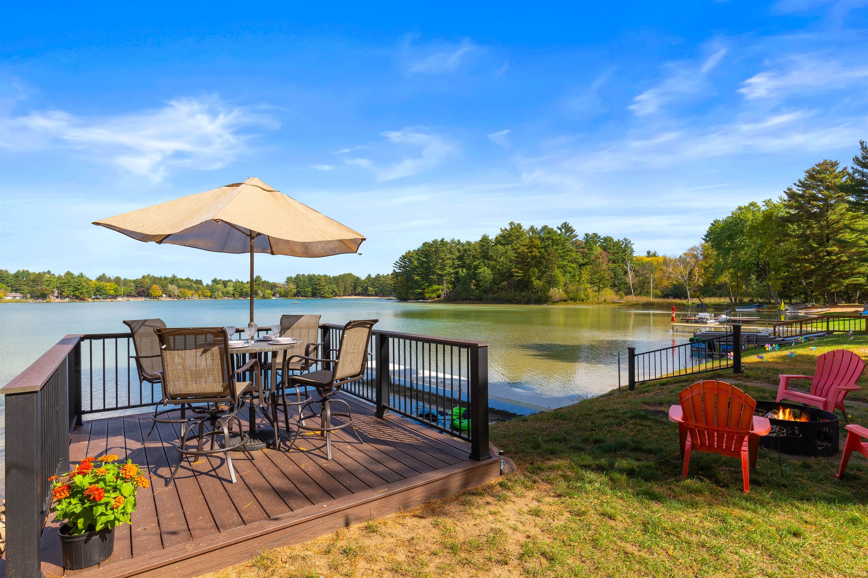 A deck with outdoor furniture, a table, and an umbrella overlooking a lake.