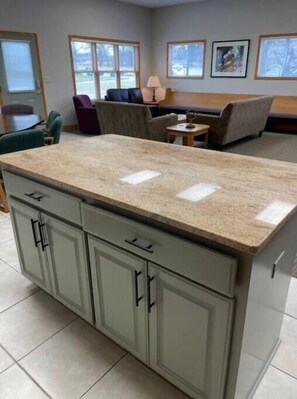 A kitchen with a granite countertop, grey cabinets, and a tiled floor.