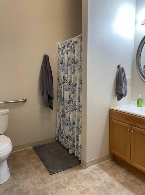 A bathroom with a toilet, shower curtain, towel rack, and wooden cabinets.