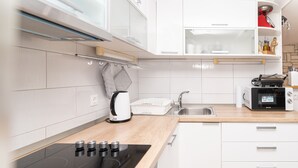 Moderni keittiö, jossa on valkoiset kaapit, musta induktioliesi, sisäänrakennettu uuni, mikroaaltouuni ja ruostumattomasta teräksestä valmistettu pesuallas.
