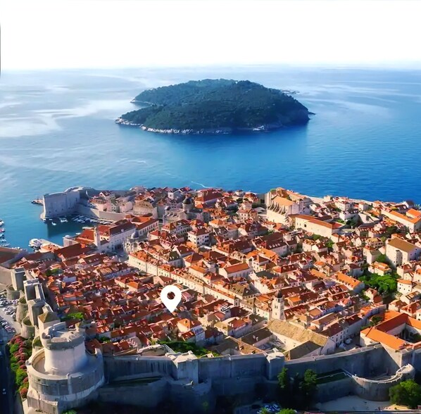 A coastal town with historic architecture, a fortified wall, and a small island in the background.