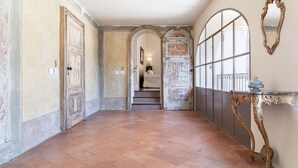 A hallway with a tiled floor, a staircase, and a decorative table with a mirror. - PM8        (Castello Cabiaglio)