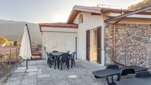 An outdoor patio with a table and chairs, a white umbrella, and a stone wall. - PM8        (Castello Cabiaglio)