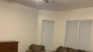 Una sala de estar con ventilador de techo, dos sofás de cuero, un aparador de madera y una ventana con persianas.
