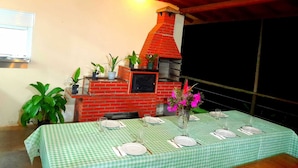 A dining area with a brick oven, green checkered tablecloths, and potted plants. - Legado das Aguas (Miracatu)