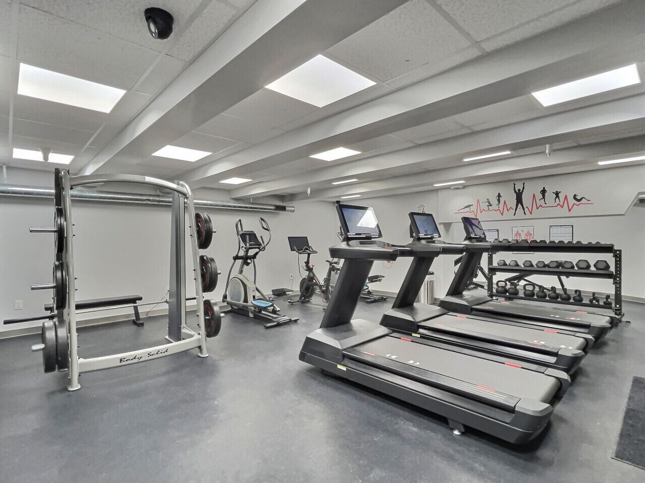 Une salle de sport équipée de tapis de course, d’un banc de musculation et d’appareils de cardio-training.