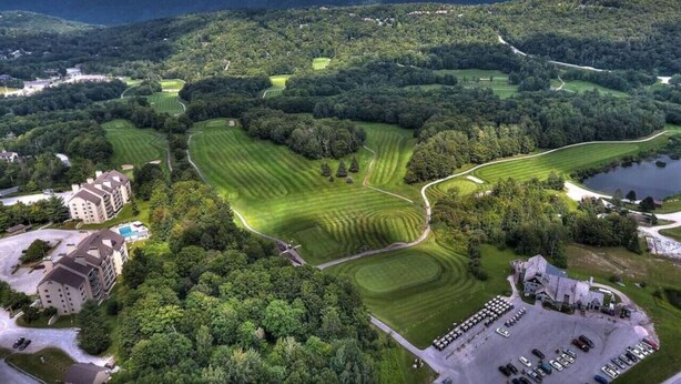 An aerial view of a golf course with multiple greens, a clubhouse, and surrounding wooded areas. - The Grizz- AC, Pool, Sauna, Gym, Near Resort (Killington)