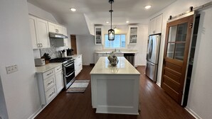 A modern kitchen with white cabinetry, stainless steel appliances, and a central island. - Spacious 5BR • Walk to Main St (Cheboygan)