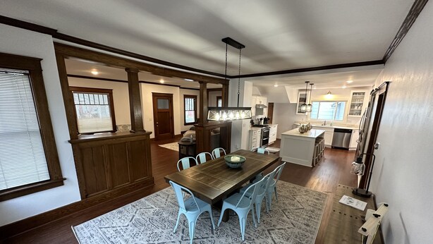 A spacious dining area with a wooden table and blue chairs, a kitchen with white cabinets, and a large island with a sink. - Spacious 5BR • Walk to Main St (Cheboygan)