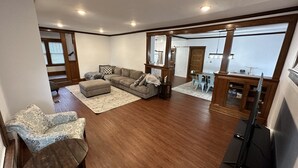 A spacious living room with a large sectional sofa, a small ottoman, and a dining area with a table and chairs. - Spacious 5BR • Walk to Main St (Cheboygan)