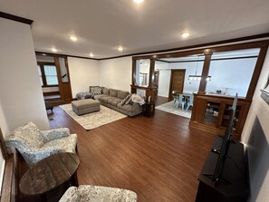A spacious living room with a large sectional sofa, a small ottoman, and a dining area with a table and chairs. - Spacious 5BR • Walk to Main St (Cheboygan)