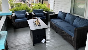 A covered outdoor seating area with wicker furniture and a table with a fire feature. - Spacious 5BR • Walk to Main St (Cheboygan)