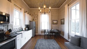A kitchen with white cabinets, a microwave, and a dining area with a table and chairs. - The Cahill- Magnolia Brewery House c 1894 (Waco)