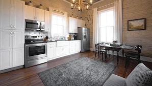 A modern kitchen with white cabinets, stainless steel appliances, a chandelier, and a dining area with a table and chairs. - The Cahill- Magnolia Brewery House c 1894 (Waco)