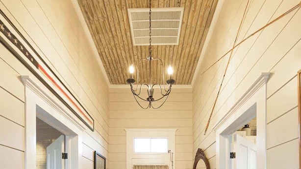 A hallway with wooden floors, white walls, and a ceiling fan. There are doors on both sides and a small table with a lamp. - The Cahill- Magnolia Brewery House c 1894 (Waco)