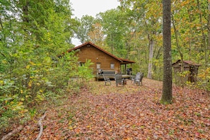Eine Hütte, umgeben von einem Wald, mit einer Terrasse und einer Sitzgelegenheit im Freien.