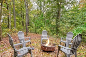 Three Adirondack chairs arranged around a metal fire pit in a forest setting. - Casa Carezza, Pet Friendly (Logan)