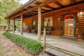 A log cabin with a porch, outdoor seating, and a covered area with a grill.