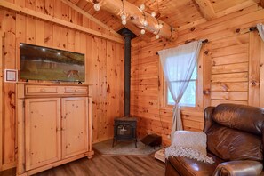 A wooden cabin interior with a television, a fireplace, a leather sofa, and a window with curtains. - Casa Carezza, Pet Friendly (Logan)