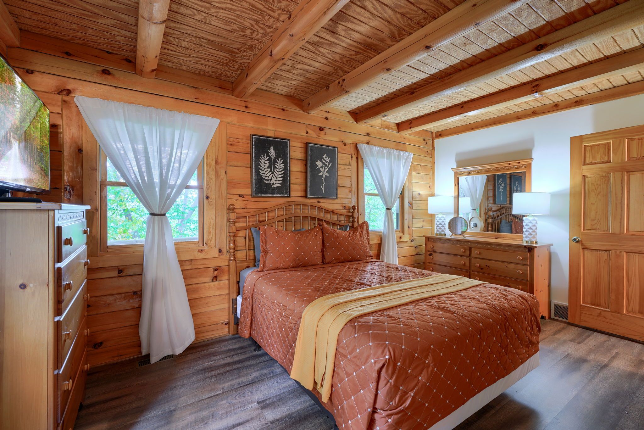 A wooden cabin bedroom with a bed, dresser, and a large mirror.
