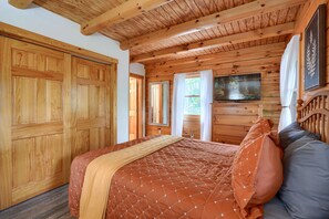 A wooden cabin bedroom with a bed, a television, and a large window.