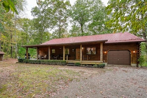 A rustic cabin with a porch, a covered seating area, and a garage.
