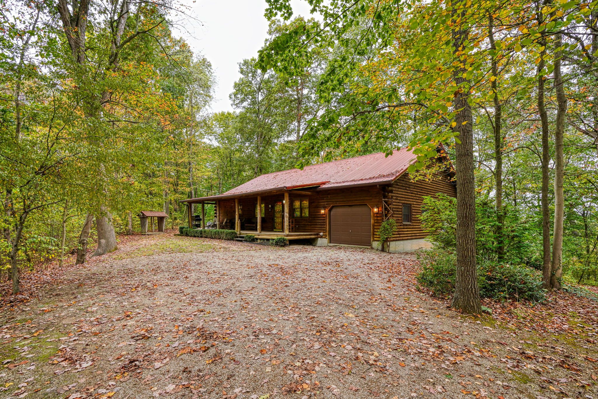 A rustic cabin with a porch, surrounded by a forest.
