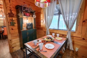 A wooden cabin interior with a dining table set for breakfast, a coffee station, and a view of the outdoors. - Casa Carezza, Pet Friendly (Logan)