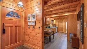 A wooden interior with a door, a kitchen area, and a dining table. - Cozy Casa Carezza Log Cabin, Logan, Ohio, Pet Friendly, Sleeps 6 (Logan)