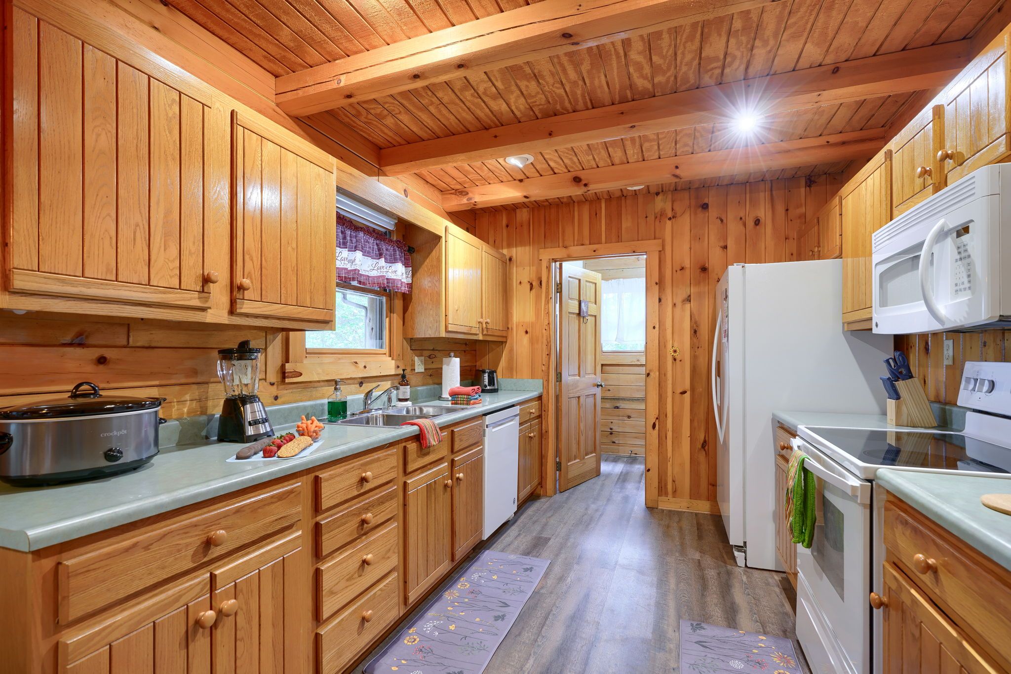 A wooden cabin-style kitchen with wooden cabinets, a refrigerator, a microwave, a stove, and a sink.