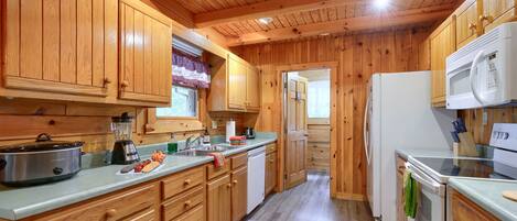 A wooden cabin-style kitchen with wooden cabinets, a refrigerator, a microwave, a stove, and a sink.