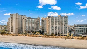 Ein Hotel direkt am Strand mit mehreren Hochhäusern, einem Sandstrand und Wellen.