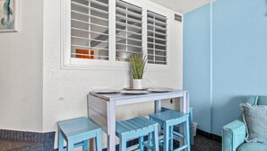 Ein kompakter Raum in Weiß und Blau mit einem kleinen Tisch, Hockern, einem Fenster mit Jalousien und einer blauen Wand.